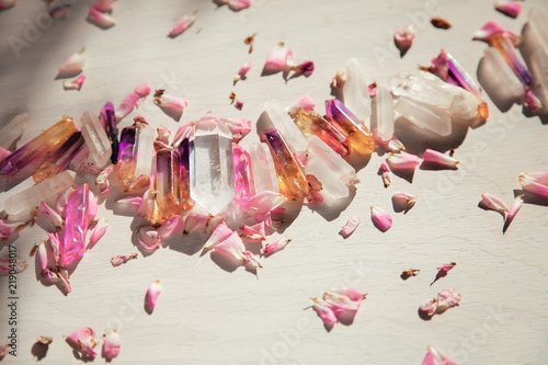 Colorful quartz crystals with pink rose leaves on wooden structure, flat lay background  