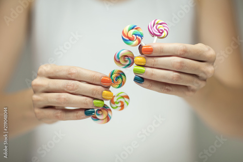 Beautiful woman hands with rainbow nail polish holding colorful swirl lollypops, funny cheerful, can be used as background  photo