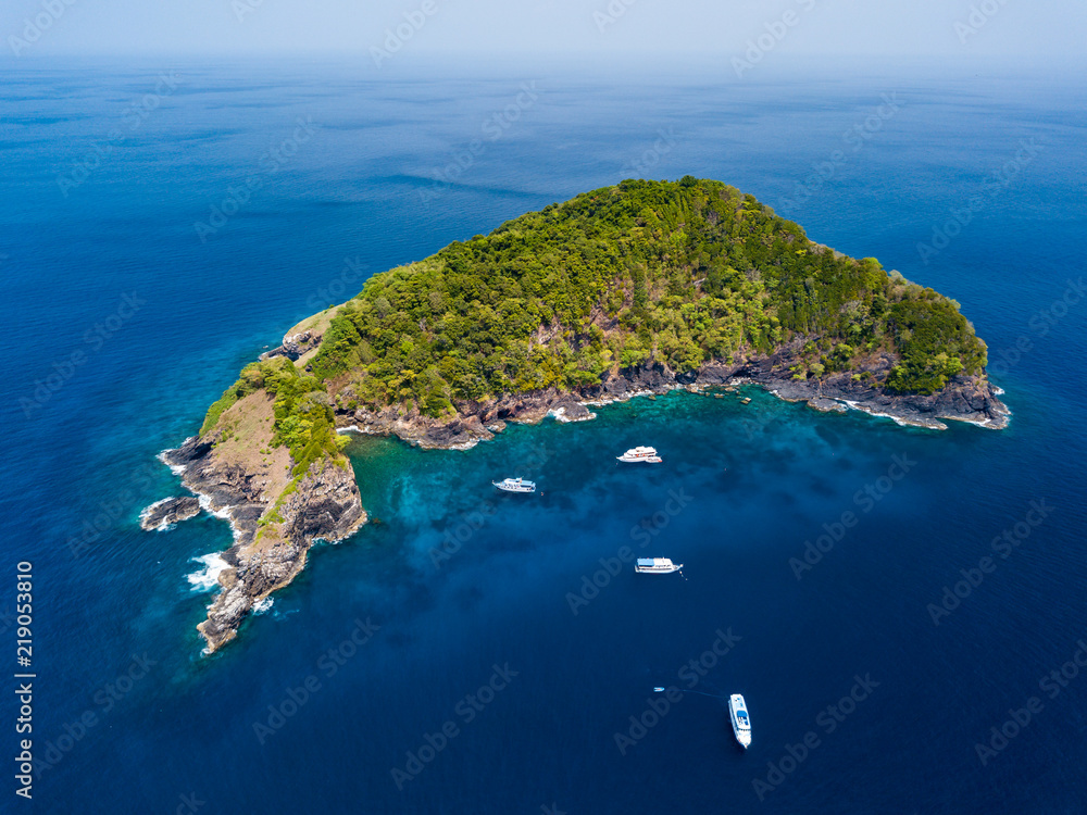 Aerial drone view of tourist boats around a beautiful, jungle covered tropical island surrounded by shallow coral reef