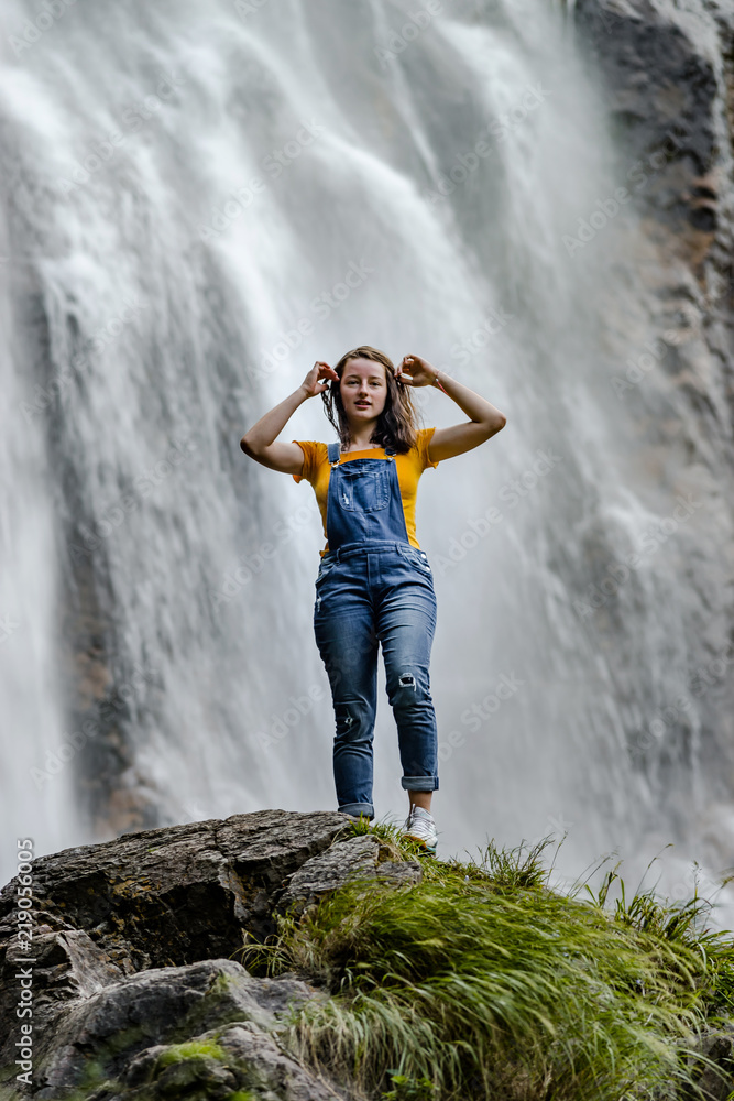 Naklejka premium Young teenage girl standing on the big stone near waterfall