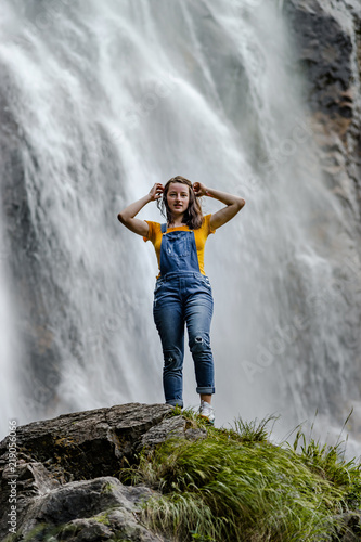 Young teenage girl standing on the big stone near waterfall