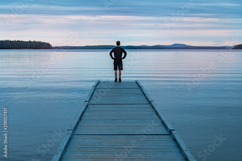 A man on a dock looking at a lake.