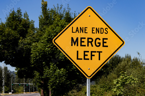 Lane ends merge left sign with trees photo