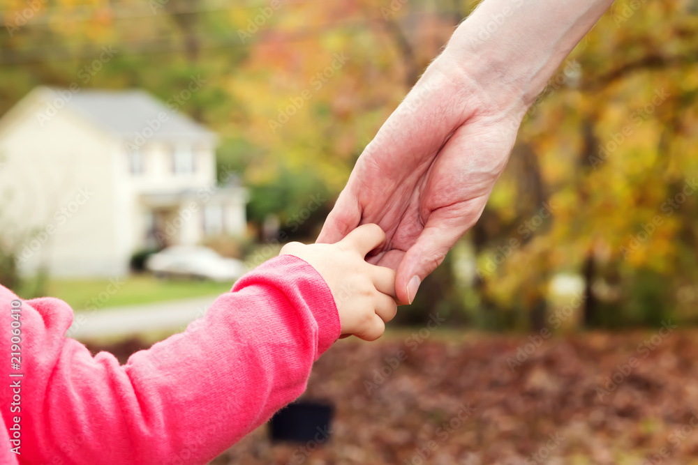 Toddler girl holding hands with her father outside on a fall day