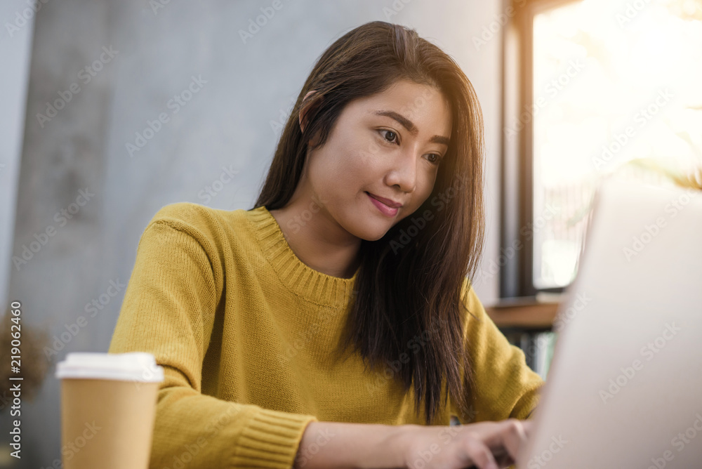 Young asian woman working with the laptop on a desk with her smile. Young woman working on weekend with her laptop in a warm sunlight day. Laptop working in the house concept. Young asian woman working with the laptop on a desk with her smile. Young woman working on weekend with her laptop in a warm sunlight day. Laptop working in the house concept.