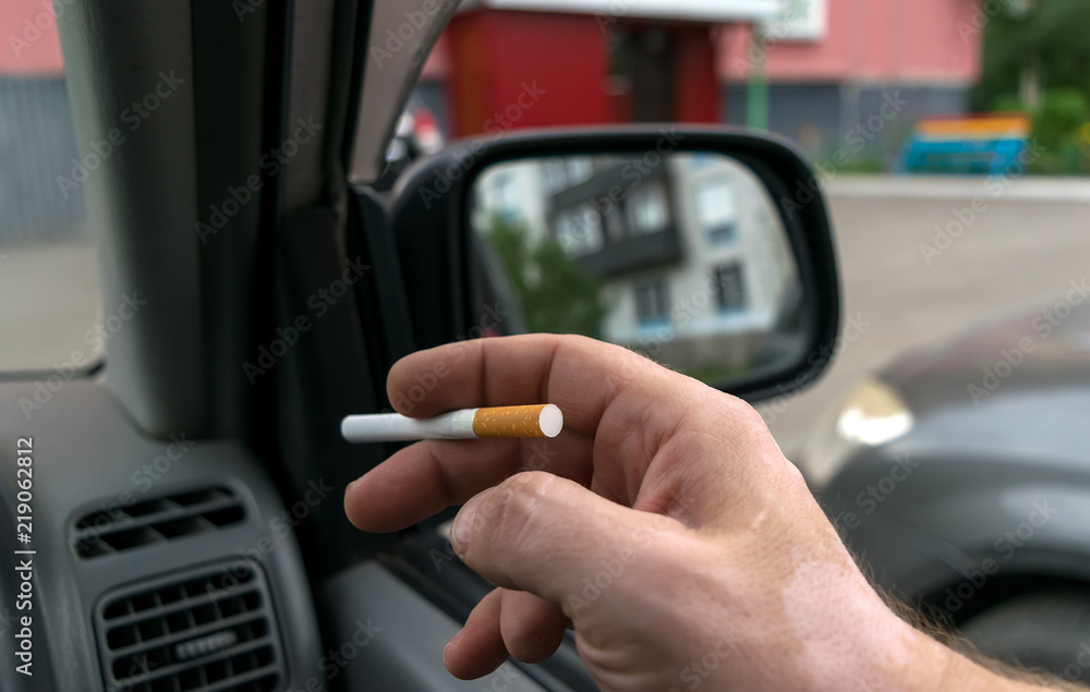 close-up of a cigarette in the hand of a man in the car, who watches the entrance door of the house