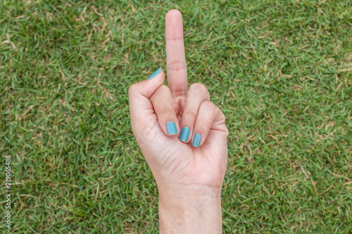 Female hand with light blue fingernails showing the middle finger on green grass © pandaclub23