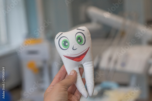 Smiling tooth in female hand on dentist office background.Tooth smiling.White healthy teeth model.Dental explorer probe with healthy tooth model. Protecting Healthy Hygienic White Tooth.Dental concept