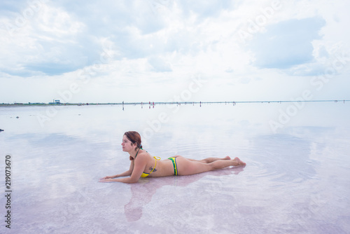 A beautiful red-haired woman in a bikini lies on her stomach in a pink salt lake. the bottom of the lake is covered with crystallized salt