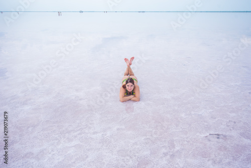 A beautiful red-haired woman in a bikini lies on her stomach in a pink salt lake. the bottom of the lake is covered with crystallized salt