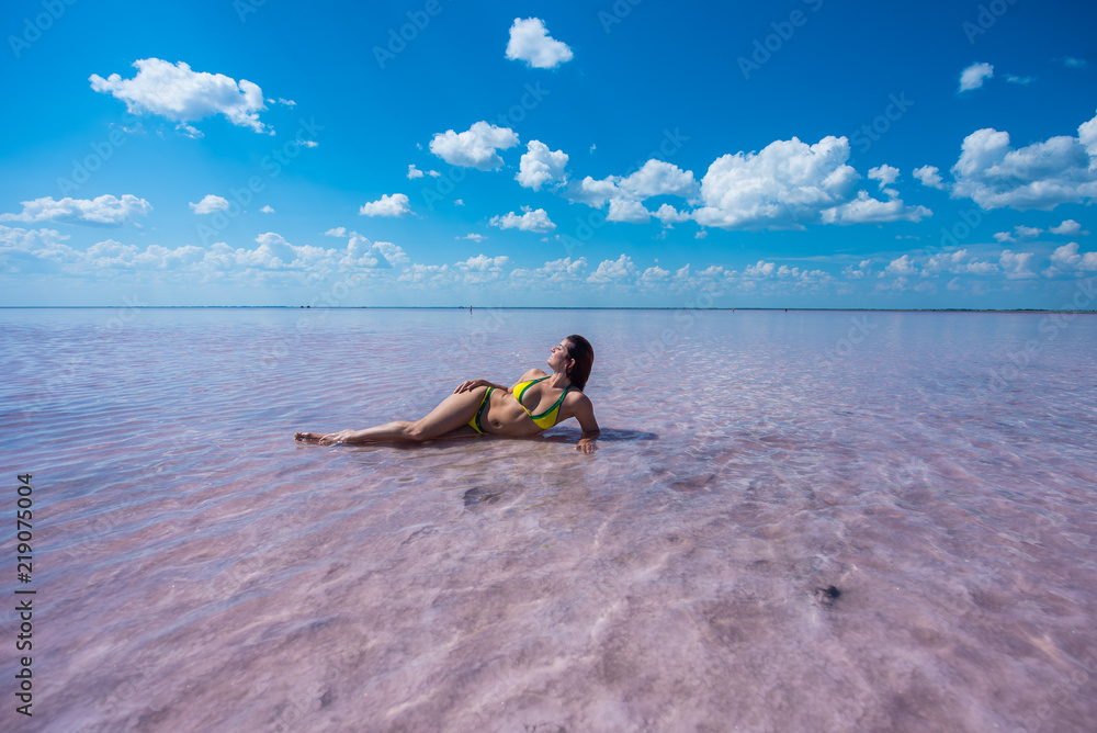 A beautiful red-haired girl in a yellow bikini lies on her side in a pink lake in Altai. Rose lake is a salt Deposit.