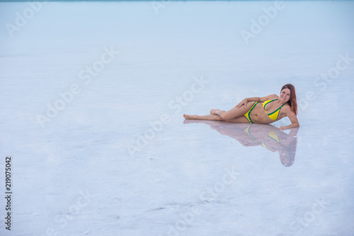 A beautiful red-haired girl in a yellow bikini lies on her side in a pink lake in Altai. Rose lake is a salt Deposit.