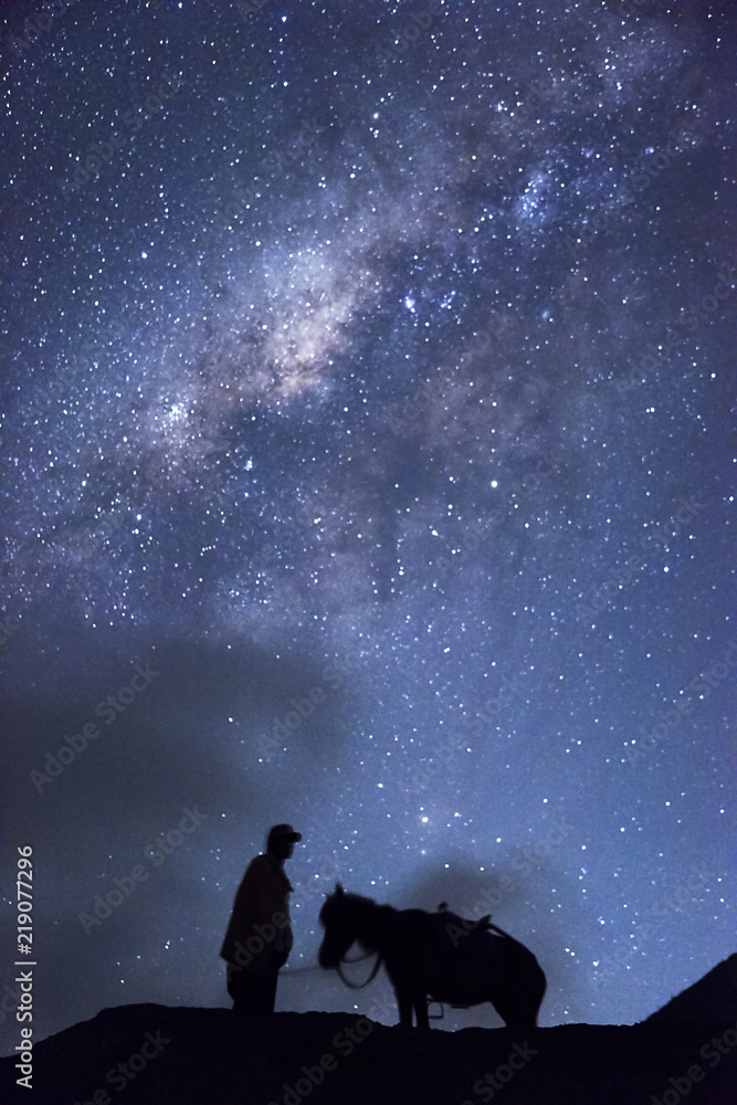 Horsemen standing under million stars in sky with his horse near smoking hot volcano Mount bromo at night, Indonesia Horsemen standing under million stars in sky with his horse near smoking hot volcano Mount bromo at night, Indonesia