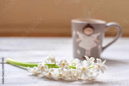 Cup of coffee and white flower on a light wooden background