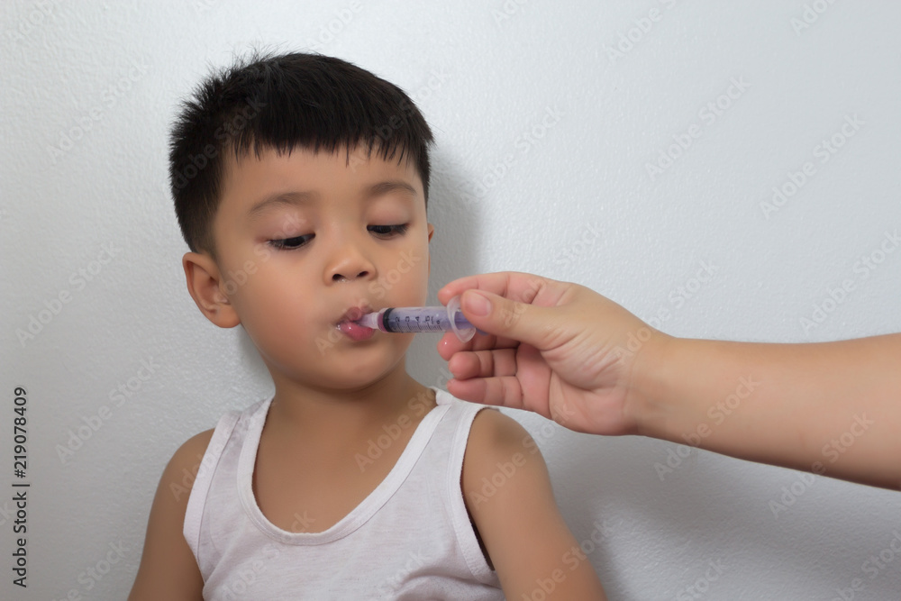 The boy is taking medication from the syringe. The boy is taking medication from the syringe.