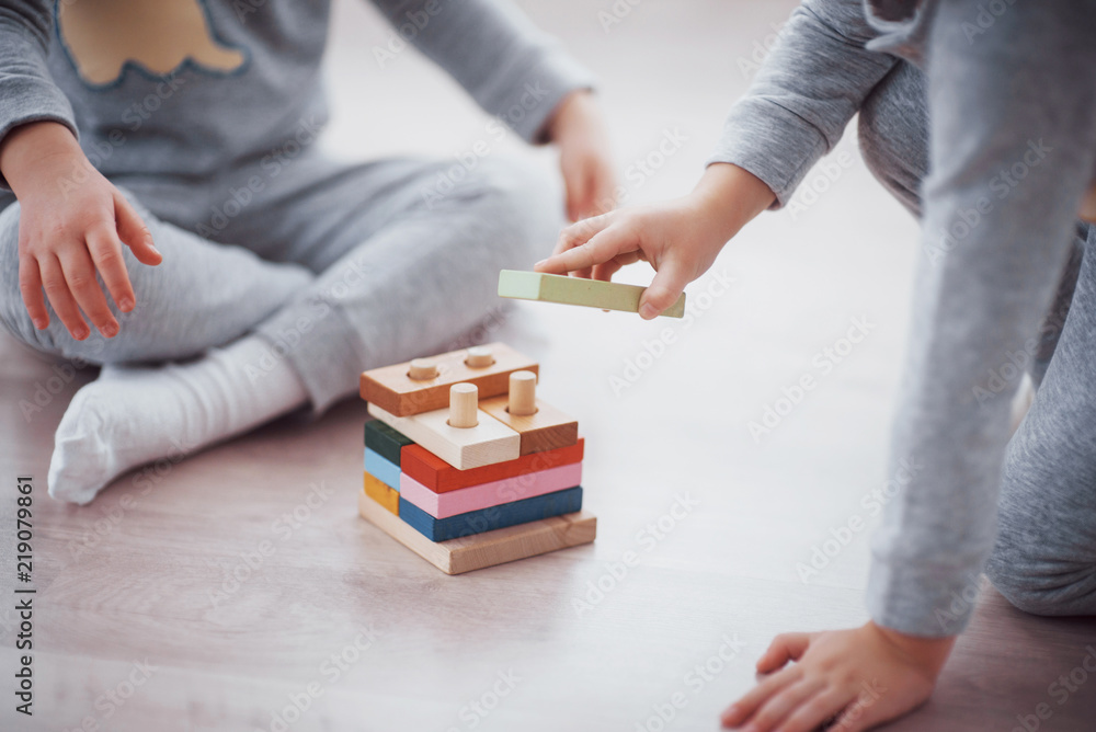 Children play with a toy designer on the floor of the children's room. Two kids playing with colorful blocks. Kindergarten educational games - obrazy, fototapety, plakaty 