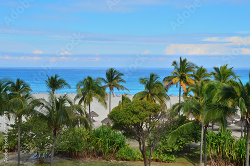 view of the Atlantic coast from the height, palm trees and vegetation, beach, beach umbrellas, figurines of people in the background near the coastline, a beautiful sky in the clouds, Varadero, Cuba