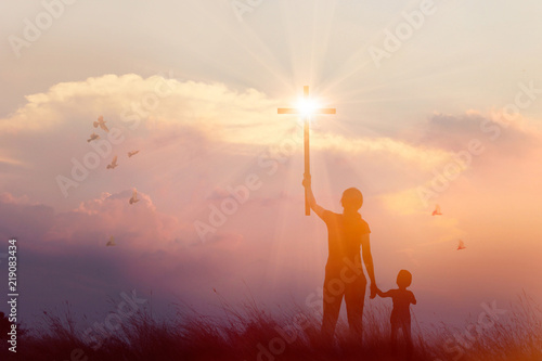 Fototapeta Naklejka Na Ścianę i Meble -  Silhouette Christianity of mother and son prayers raising cross on sunset background