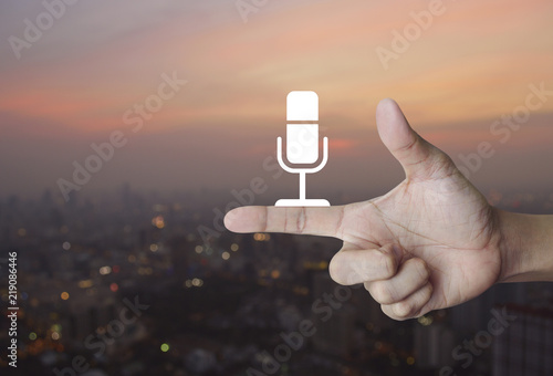 Microphone flat icon on finger over blur of cityscape on warm light sundown, Business communication concept