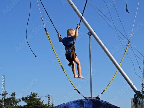 Young Little Boy on Ropes Trampoline Jumping with Sky in Background and Having Fun