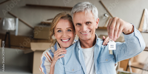 happy senior couple holding keys from new apartment and smiling at camera