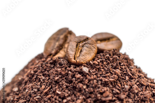 Coffee beans on pile of ground coffee. Close up. Isolated on white.