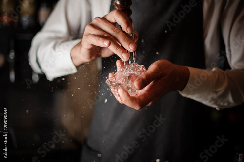 Male bartender breaking an ice cube with a special tool © fesenko