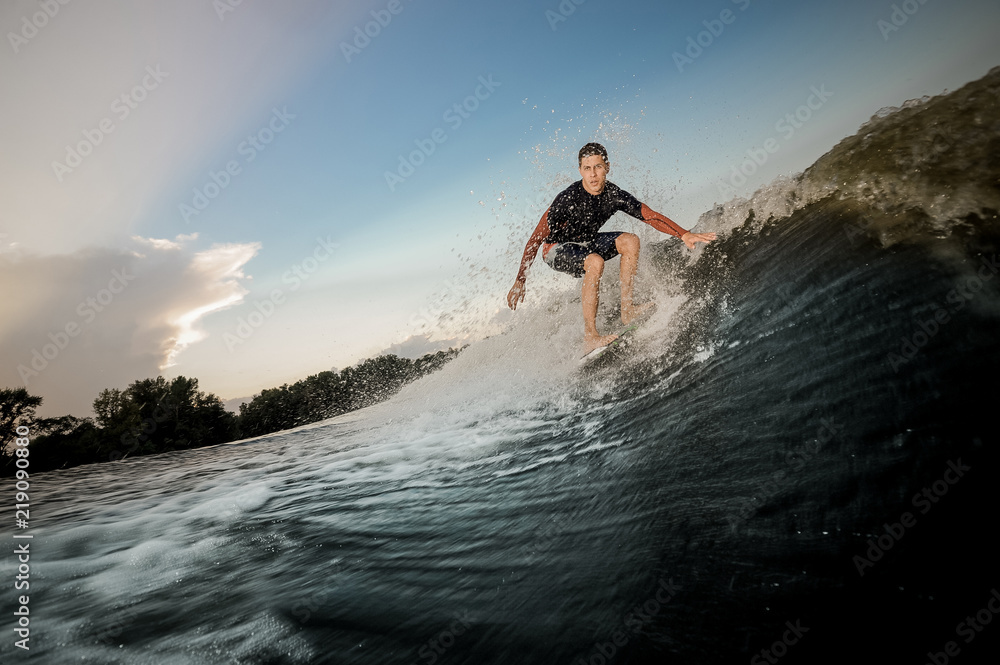Young active brunet man riding on the wakeboard on the bending knees