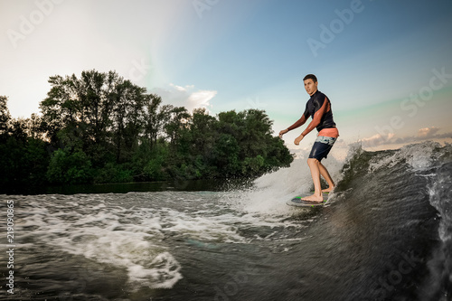 Young active brunet man riding on the wakeboard on the lake