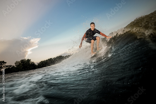 Young active brunet man riding on the wakeboard on the bending knees