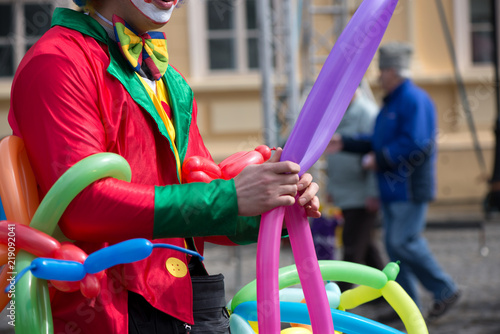 A freelance clown creating balloon animals and different shapes at outdoor festival in city center. School bag, angel wings, butterflies and dogs made of balloons. Concept of entertainment, birthdays