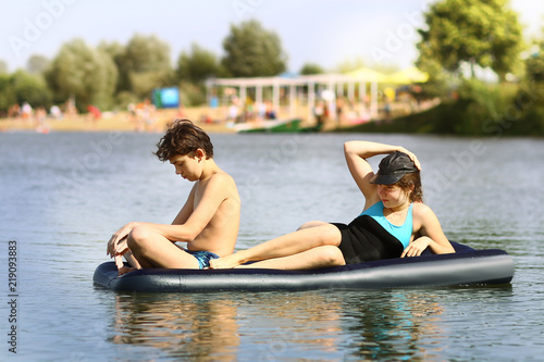 siblings brother and sister with inflatable matrass swim in the lake on sand beach background photo