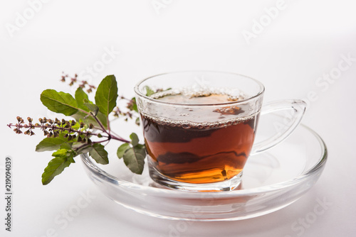 pouring Holy Basil or Tulsi Tea in transparent glass cup with saucer over white or black background. Popular Ayurvedic medicine from India