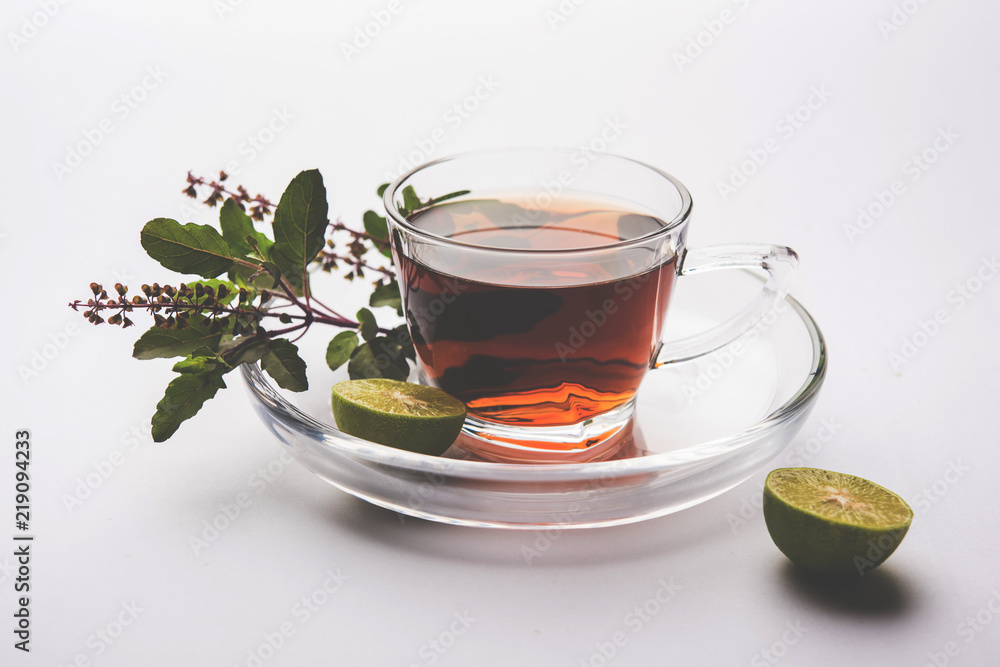 pouring Holy Basil or Tulsi Tea in transparent glass cup with saucer over white or black background. Popular Ayurvedic medicine from India pouring Holy Basil or Tulsi Tea in transparent glass cup with saucer over white or black background. Popular Ayurvedic medicine from India