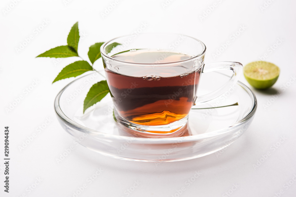pouring Neem tea in transparent glass cup with saucer over white background. Popular Ayurvedic medicine from India
