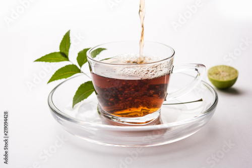 pouring Neem tea in transparent glass cup with saucer over white background. Popular Ayurvedic medicine from India