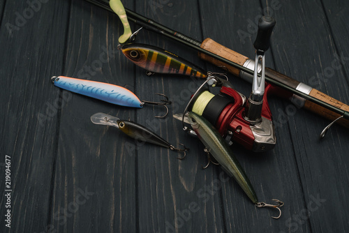 Fishing tackle - fishing spinning, hooks and lures on darken wooden background. Top view. photo