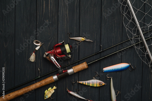 Fishing tackle - fishing spinning, hooks and lures on darken wooden background. Top view. photo