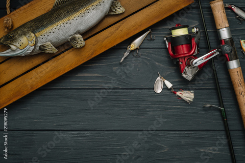 Fishing tackle - fishing spinning, hooks and lures on darken wooden background. Top view. photo