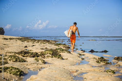 back view of sportsman with surfing board walking on sandy beach