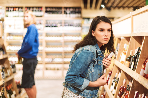 Foto Young serious woman in denim jacket frightenedly looking aside while trying stea