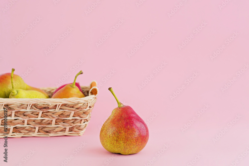Ripe pears in wicker basket on pale pink background Ripe pears in wicker basket on pale pink background