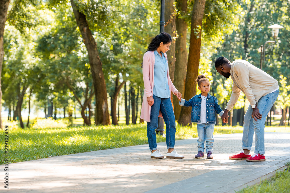 african american parents and daughter holding hands in park, father looking at daughter african american parents and daughter holding hands in park, father looking at daughter