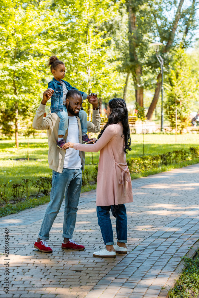 happy african american father holding daughter on shoulders in park