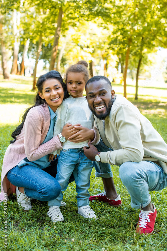 smiling african american parents and daughter looking at camera in park