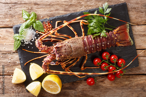Raw spiny lobster with tomato, lemon and herbs close up on a black board. Horizontal top view photo