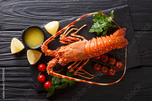 Fotografia Expensive food: spiny boiled lobster with fresh tomato, lemon and melted butter close-up on black stone