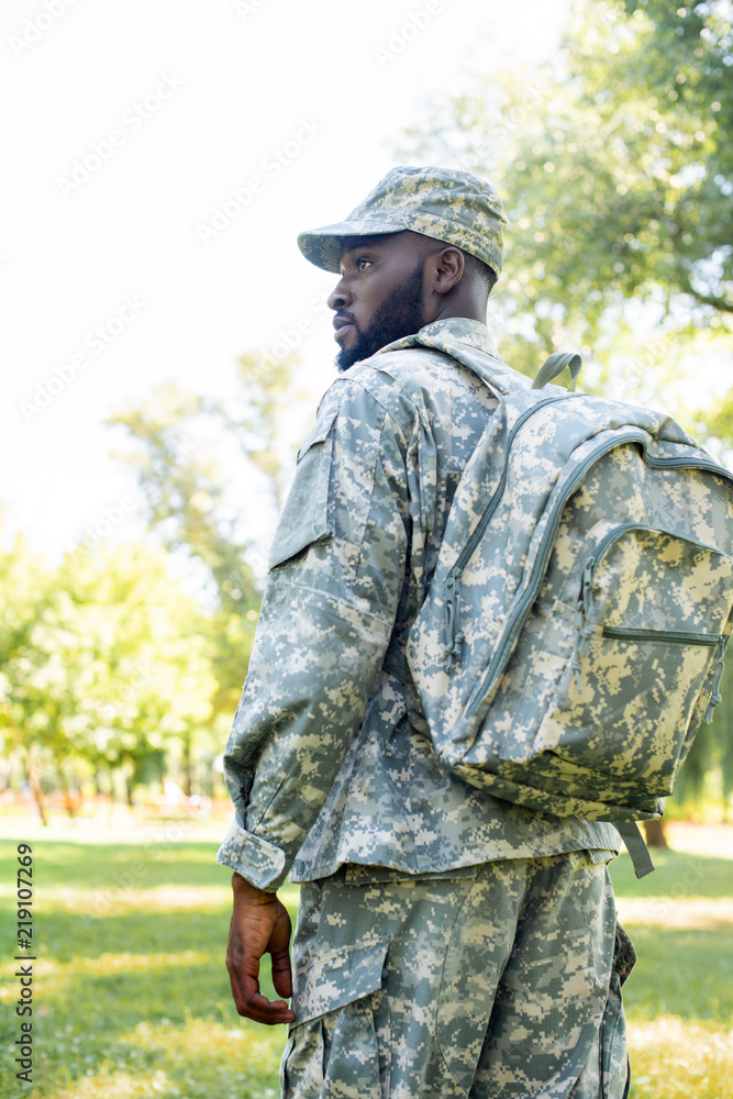 low angle view of african american soldier in military uniform and bag looking away in park
