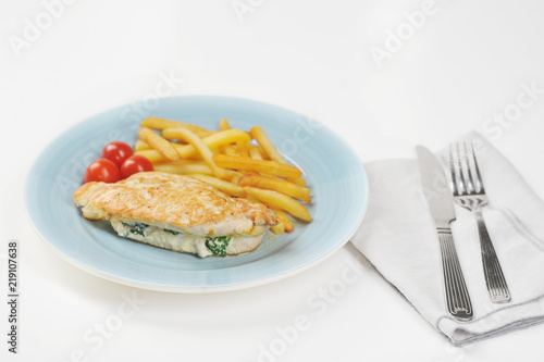 On the plate is a chicken breast stuffed with spinach and ricotta. Next to the plate is a glass of water, a napkin and cutlery. Light background. Close-up.