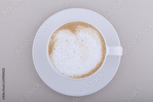 White cup of cappuccino with foam on textile background
